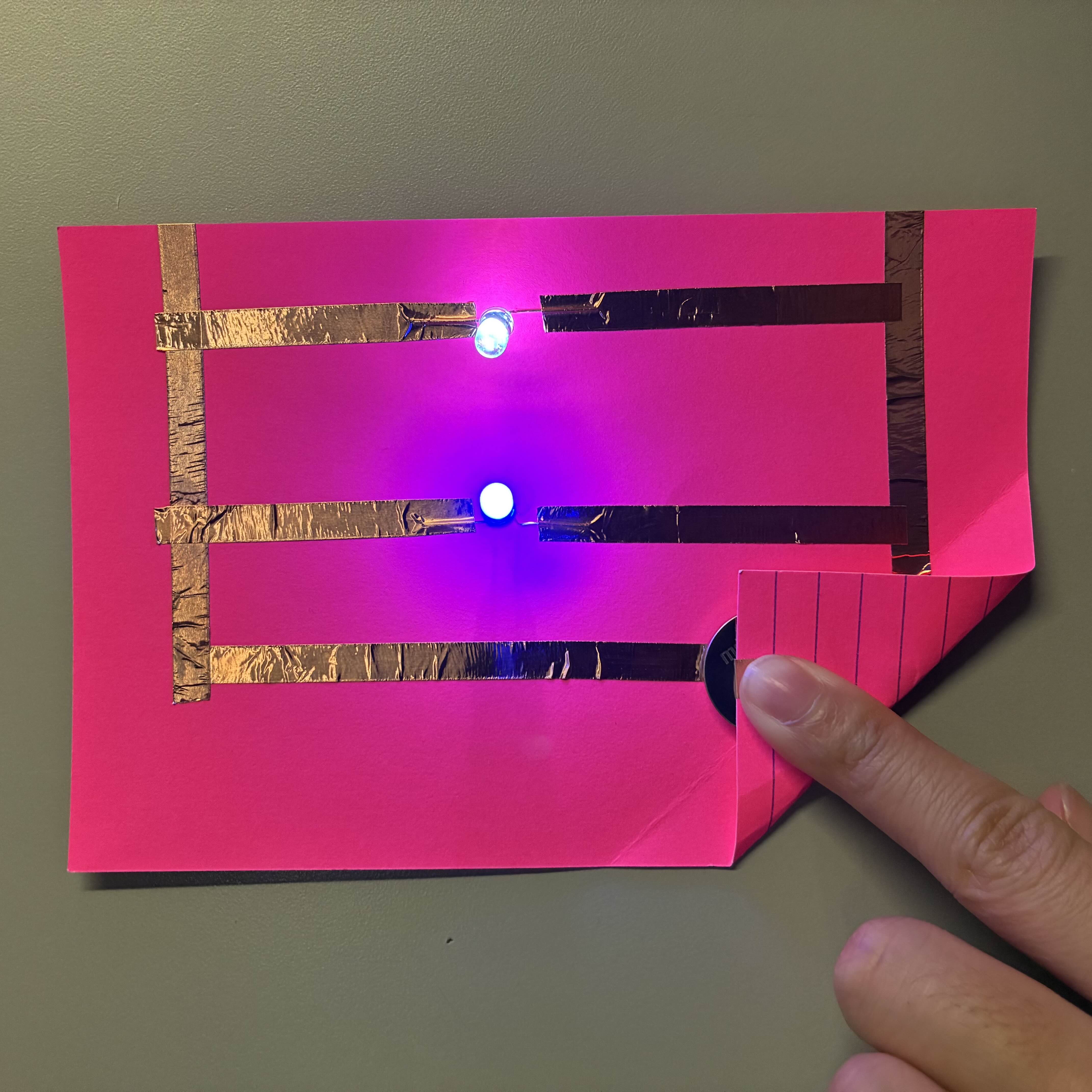 This is my parallel circuit with the battery connecting the copper tape to make both the lights turn on at the same time. I used blue and white lights to contrast the pink background.